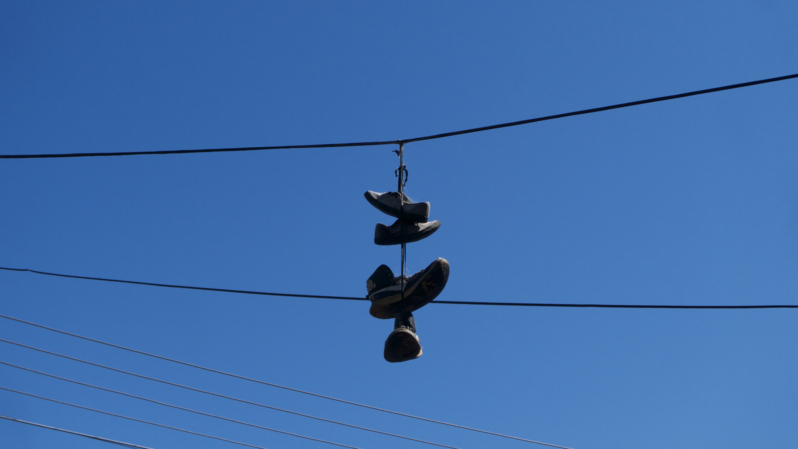 Deux paires de chaussures accrochées par leurs lacets à un câble, le ciel bleu en fond